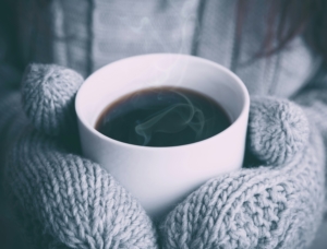 Mug of coffee held by hands wearing mittens